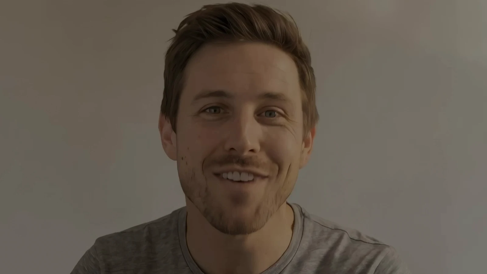 A finished frame from the film: the presenter smiling straight to camera against a plain, softly lit wall.