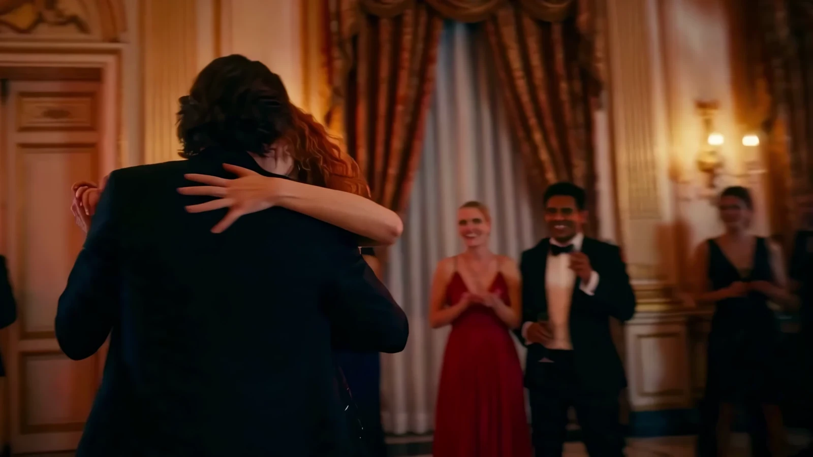 A finished frame from the film: a couple embracing in a warmly lit ballroom as guests applaud.